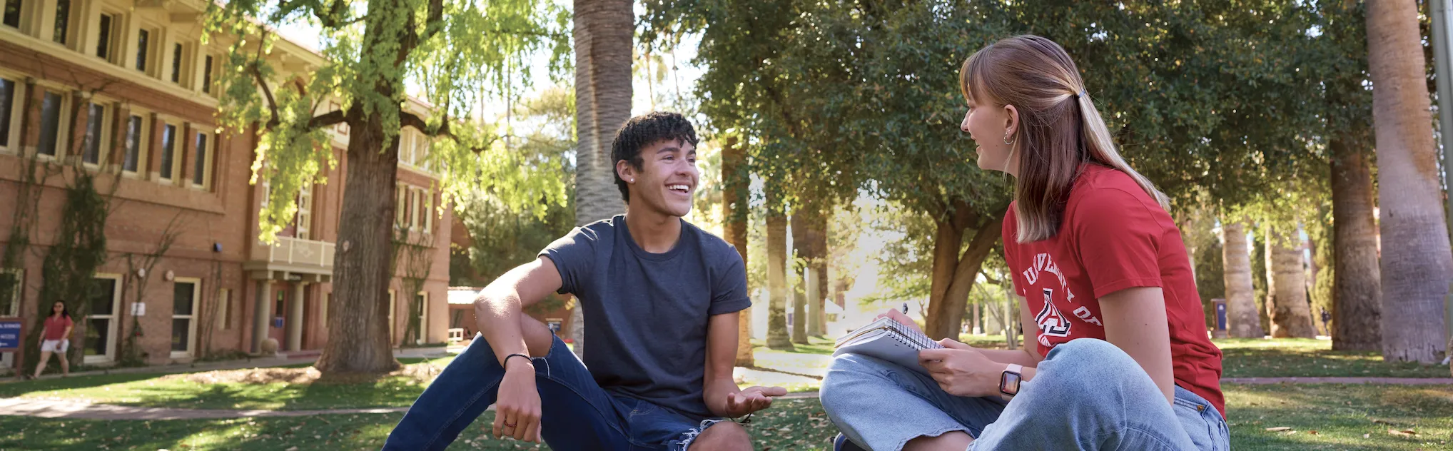 A boy and girl student sitting on the grass on campus